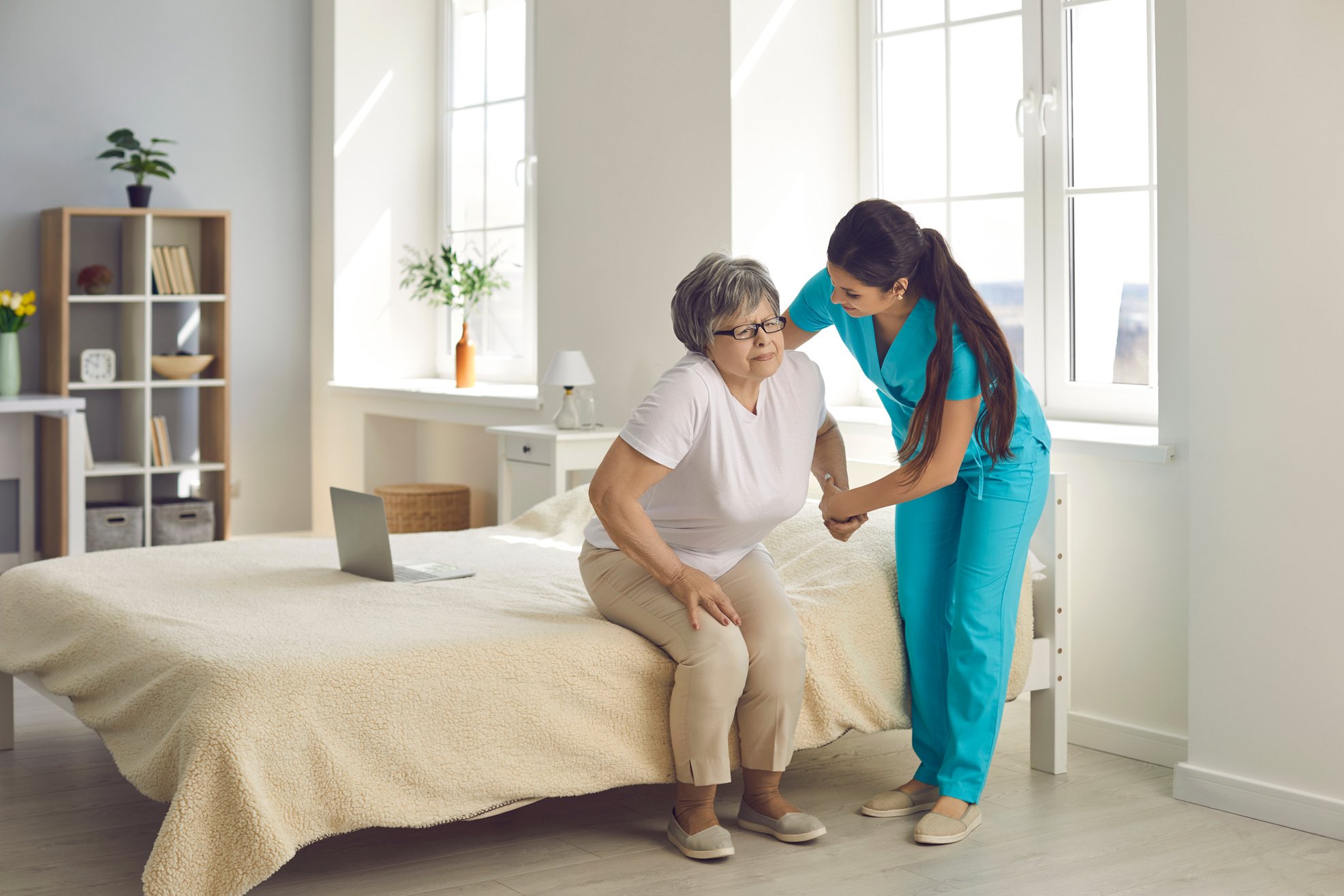 Female Caregiver Who Cares for an Elderly Woman in a Nursing Home Helps Her Get Out of Bed.